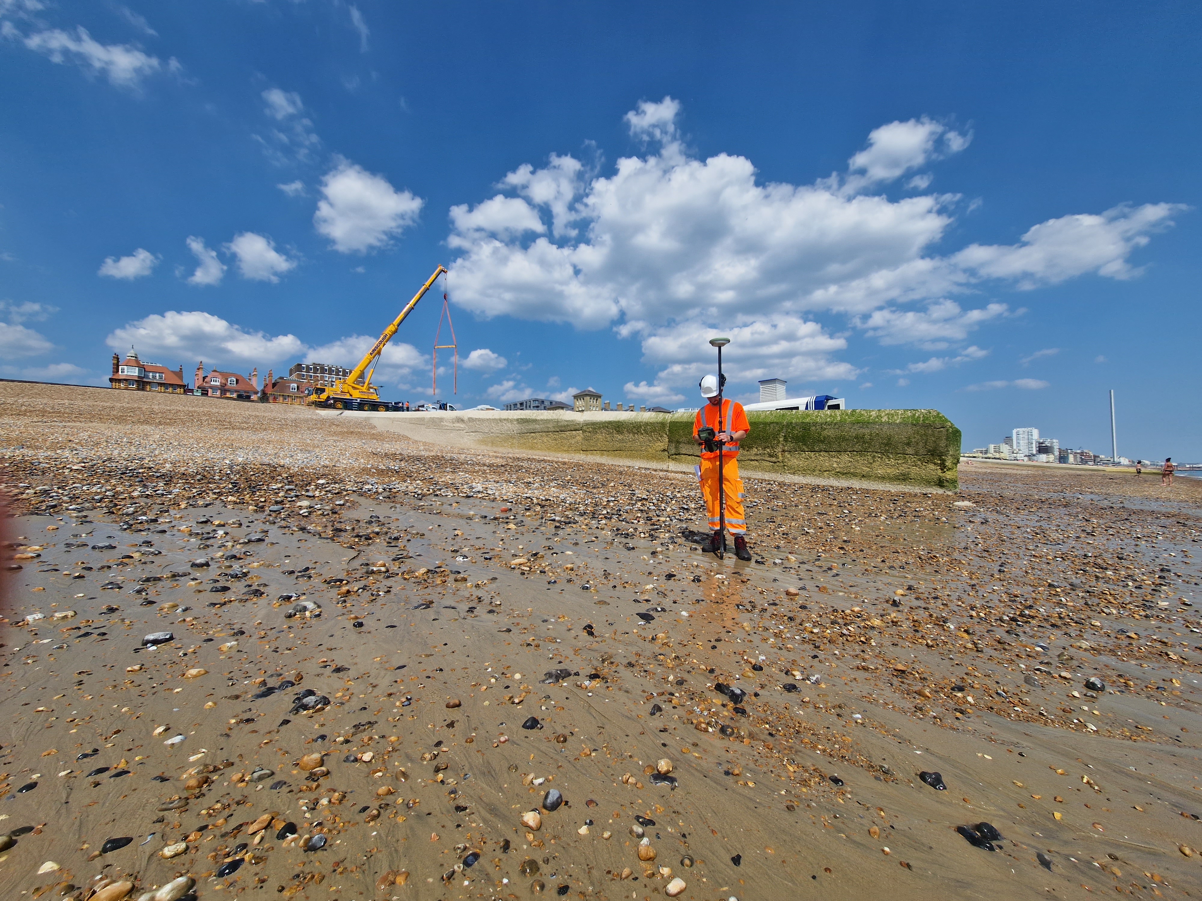 Site operative on Brighton Beach using a GPS for borehole location surveying with a Crain in the background 